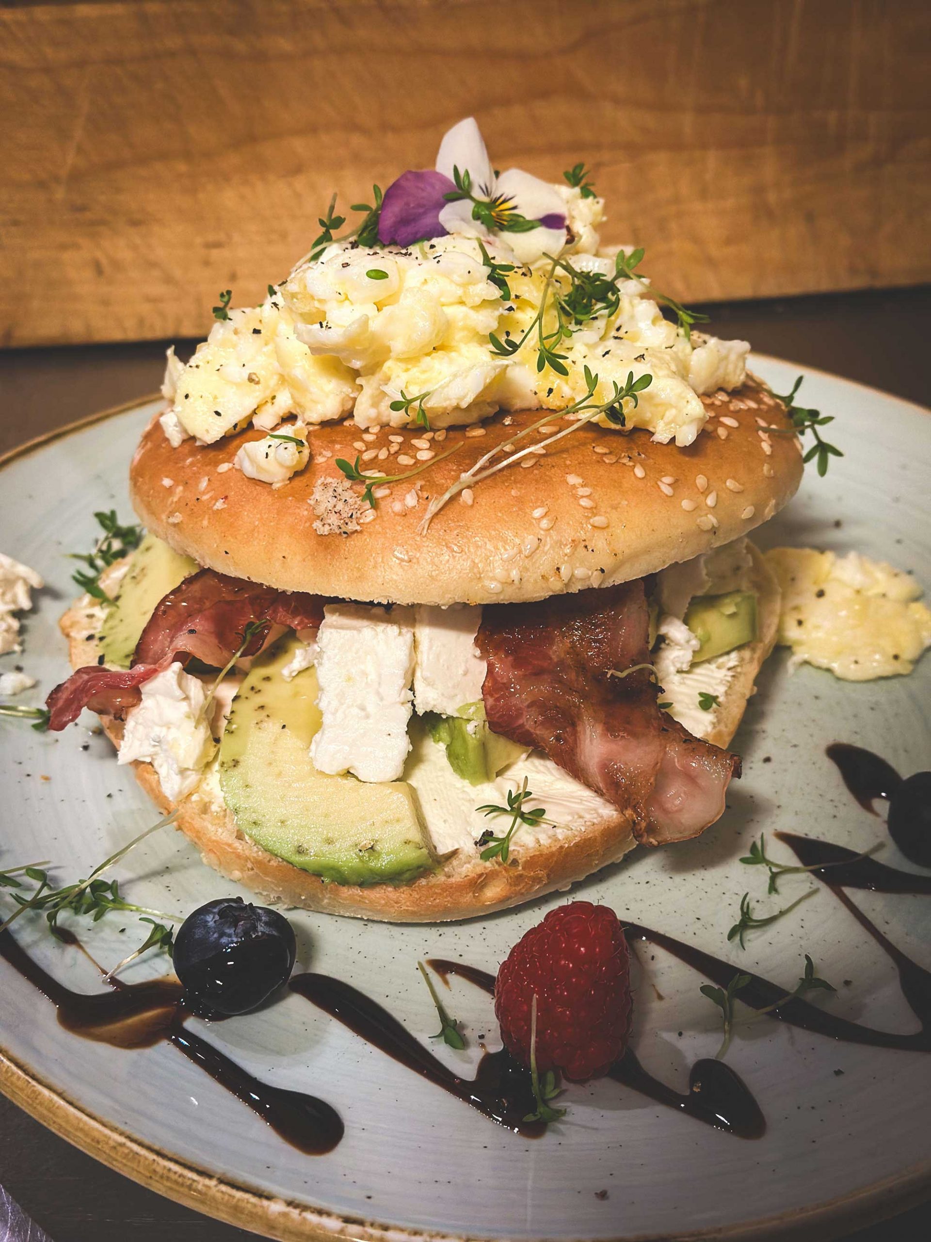 Frühstücks-Bagel mit Avocado, Speck, Rührei hübsch dekoriert mit Früchten