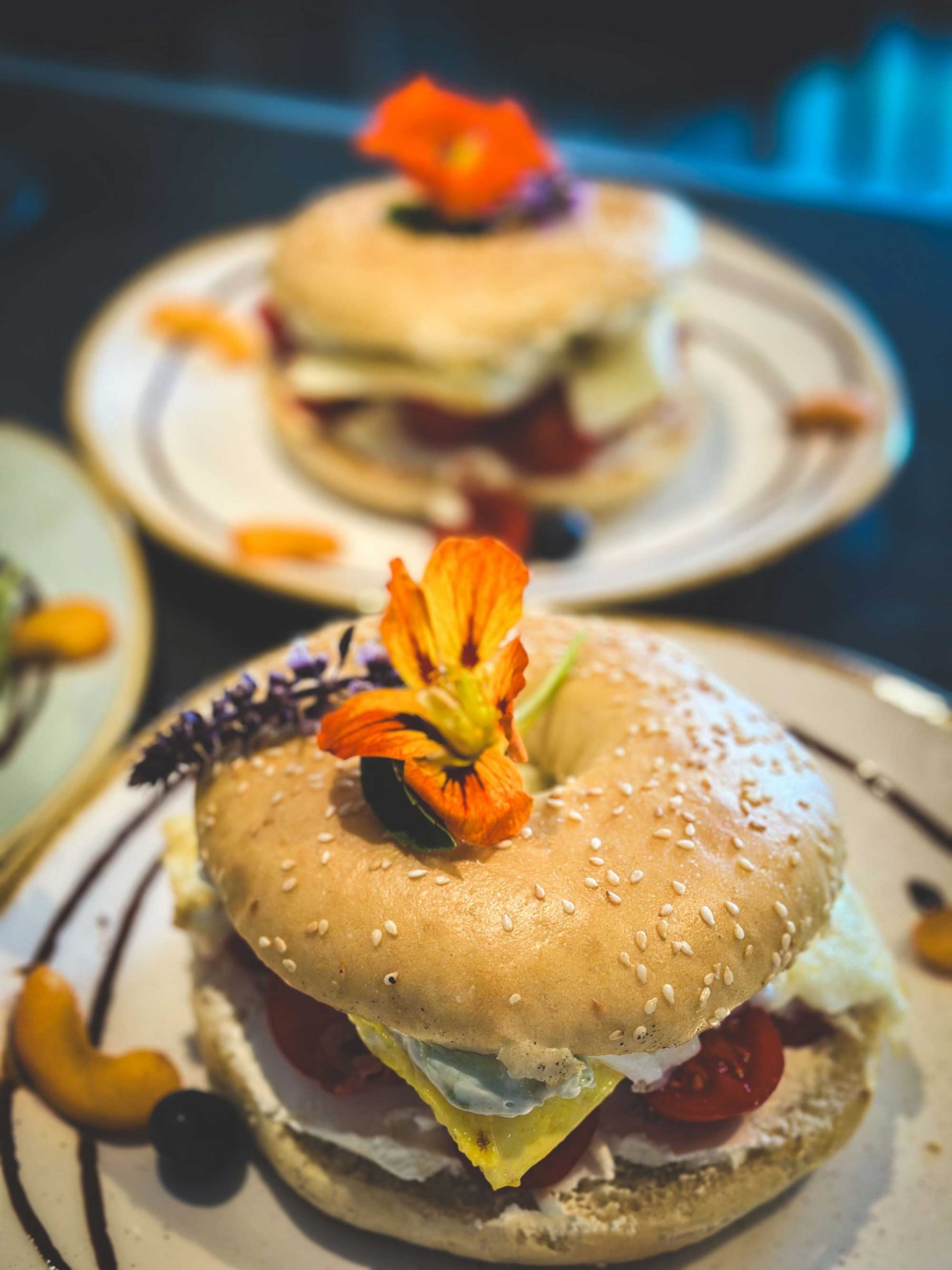 Frühstücks-Bagel mit Ei, Käse, Tomaten hübsch dekoriert auf einem Teller mit Früchten und Essblumen