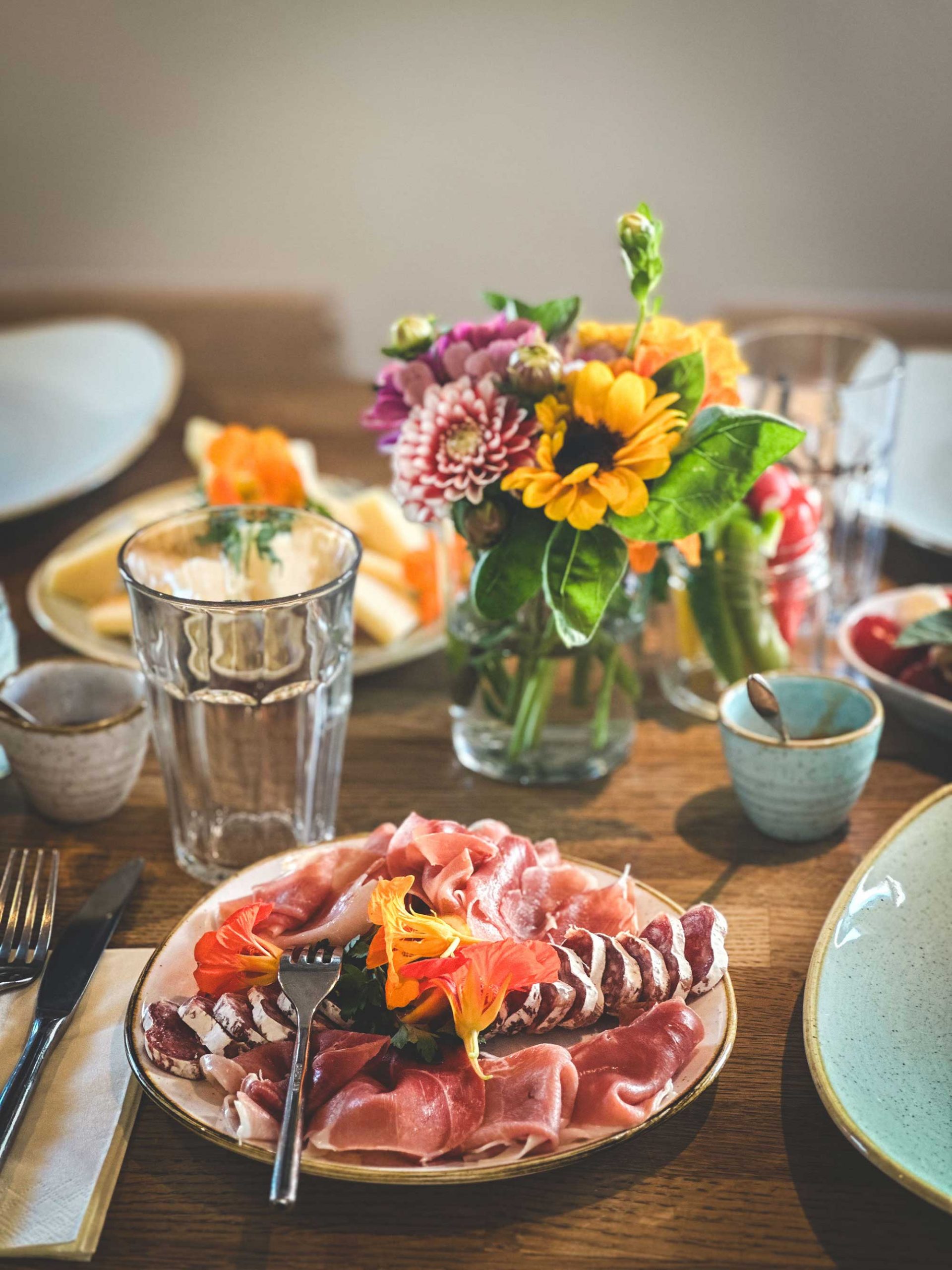 Hübsch gedeckter Frühstückstisch mit Blumenstrauss, Wurst- und Käseplatte