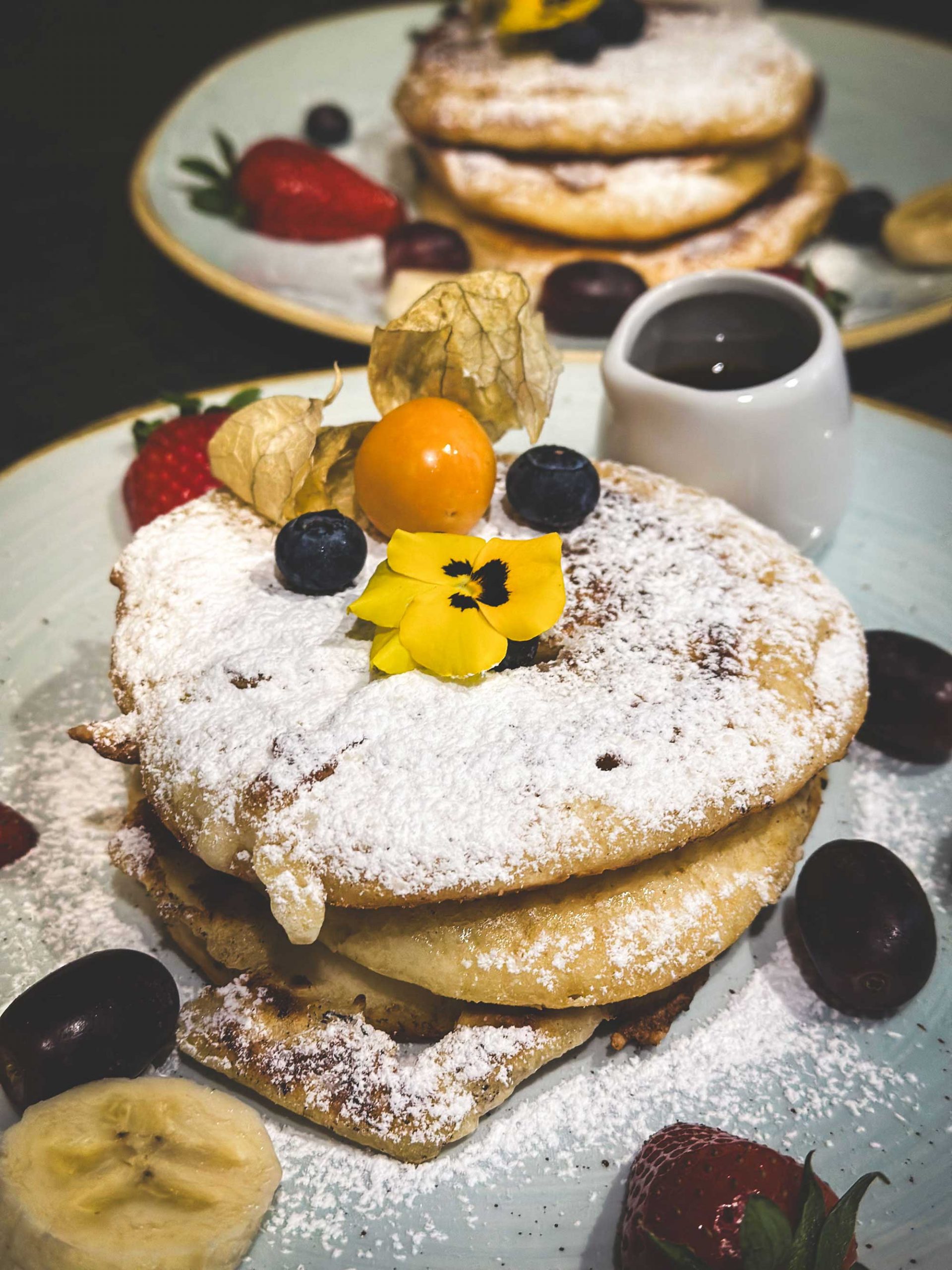 Hübsch dekorierter Teller mit Pancakes und frischen Früchten sowie Essblumen